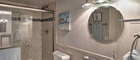 A modern bathroom with a glass-enclosed shower, a round mirror, and a glass bowl sink.