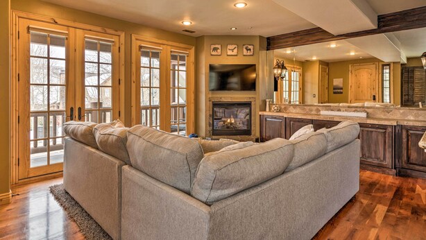 A spacious living room with a large sectional sofa, a fireplace, and a kitchen area with wooden cabinets and a stone countertop.