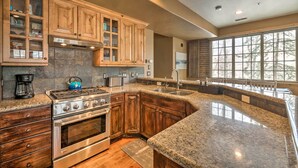 A kitchen with wooden cabinets, granite countertops, a stove, and a large window providing natural light.