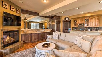 A spacious living room with a fireplace, a large sofa, and a kitchen area with wooden cabinets and a stone countertop.