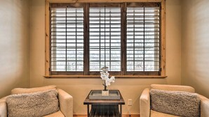 A room with two beige armchairs, a small table with a vase of white flowers, and a window with blinds.