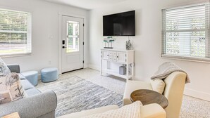 Ein modernes Wohnzimmer mit einer weißen Tür, einem flachbildfernseher an der Wand und einer Sitzecke mit Sofa und Hocker.