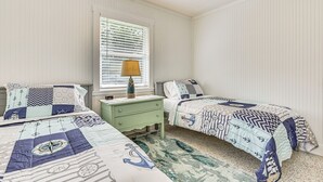 Ein Schlafzimmer mit zwei Betten, einem Nachttisch, einem Fenster mit Jalousien und einem Deckenventilator.
