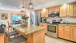 A modern kitchen with granite countertops, wooden cabinets, stainless steel appliances, and a central island with seating.