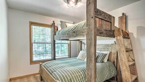 A bunk bed with a wooden ladder, a window with blinds, and a light fixture above the bed.