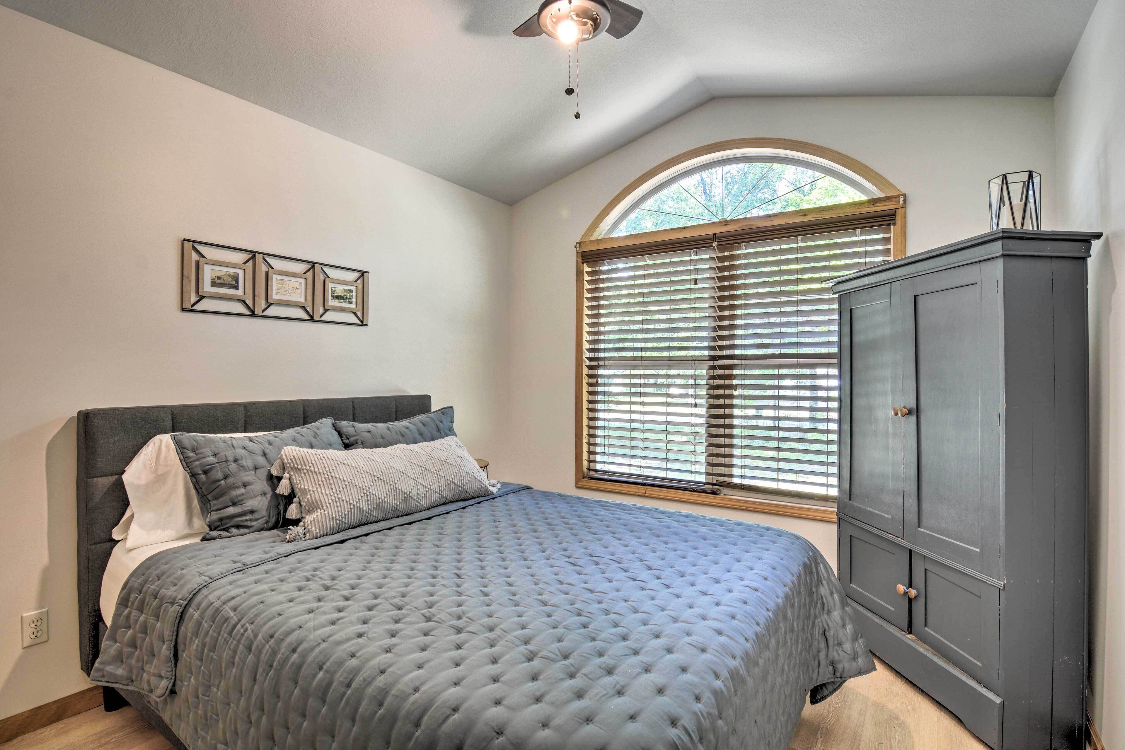 A bedroom with a bed, a wardrobe, a window with blinds, and a ceiling fan.