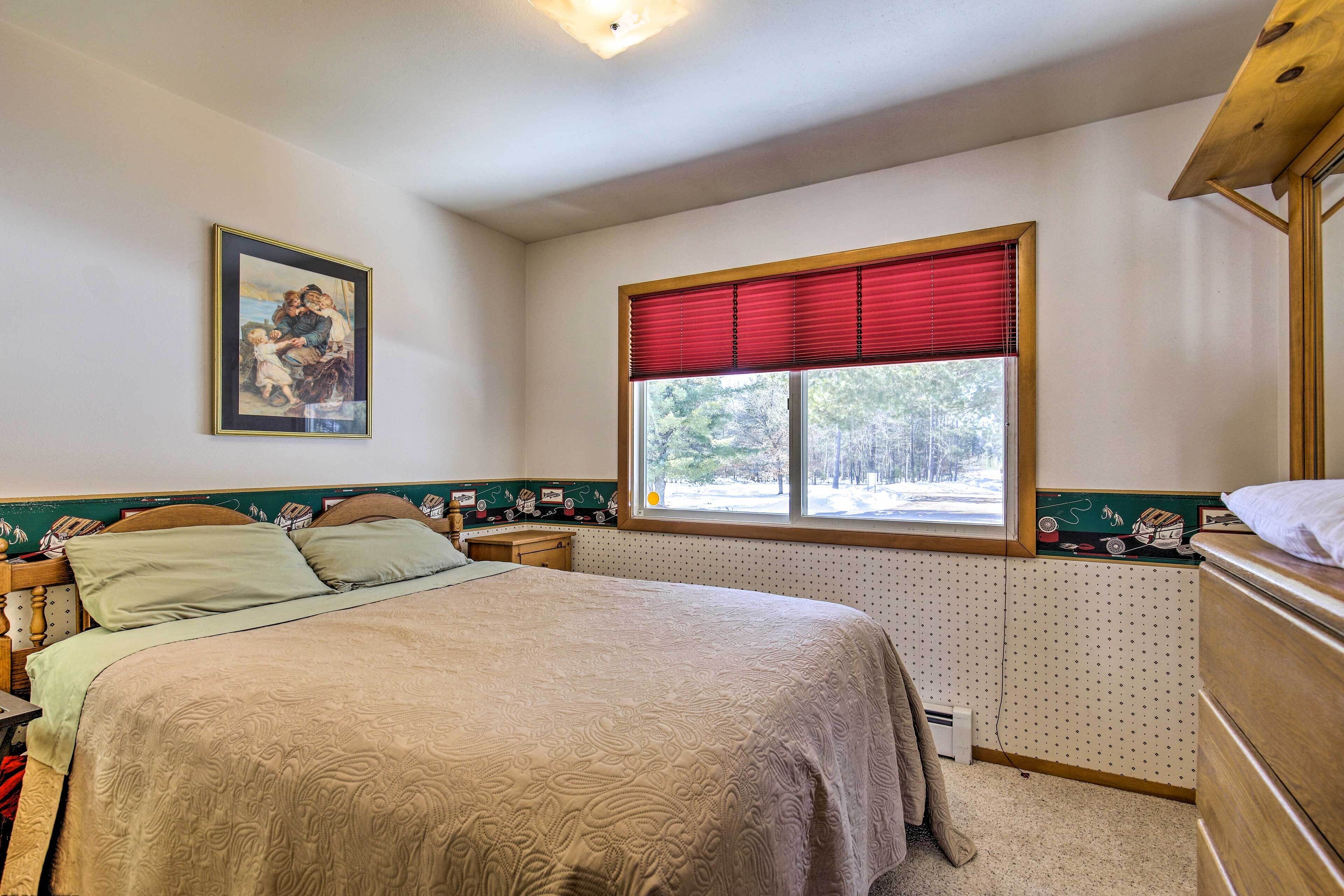 A bedroom with a bed, a window with red blinds, a wall-mounted telephone, and a framed picture on the wall.