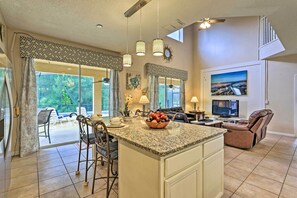 A spacious kitchen with a granite countertop, a bowl of fruit, and a dining area with chairs and a table.
