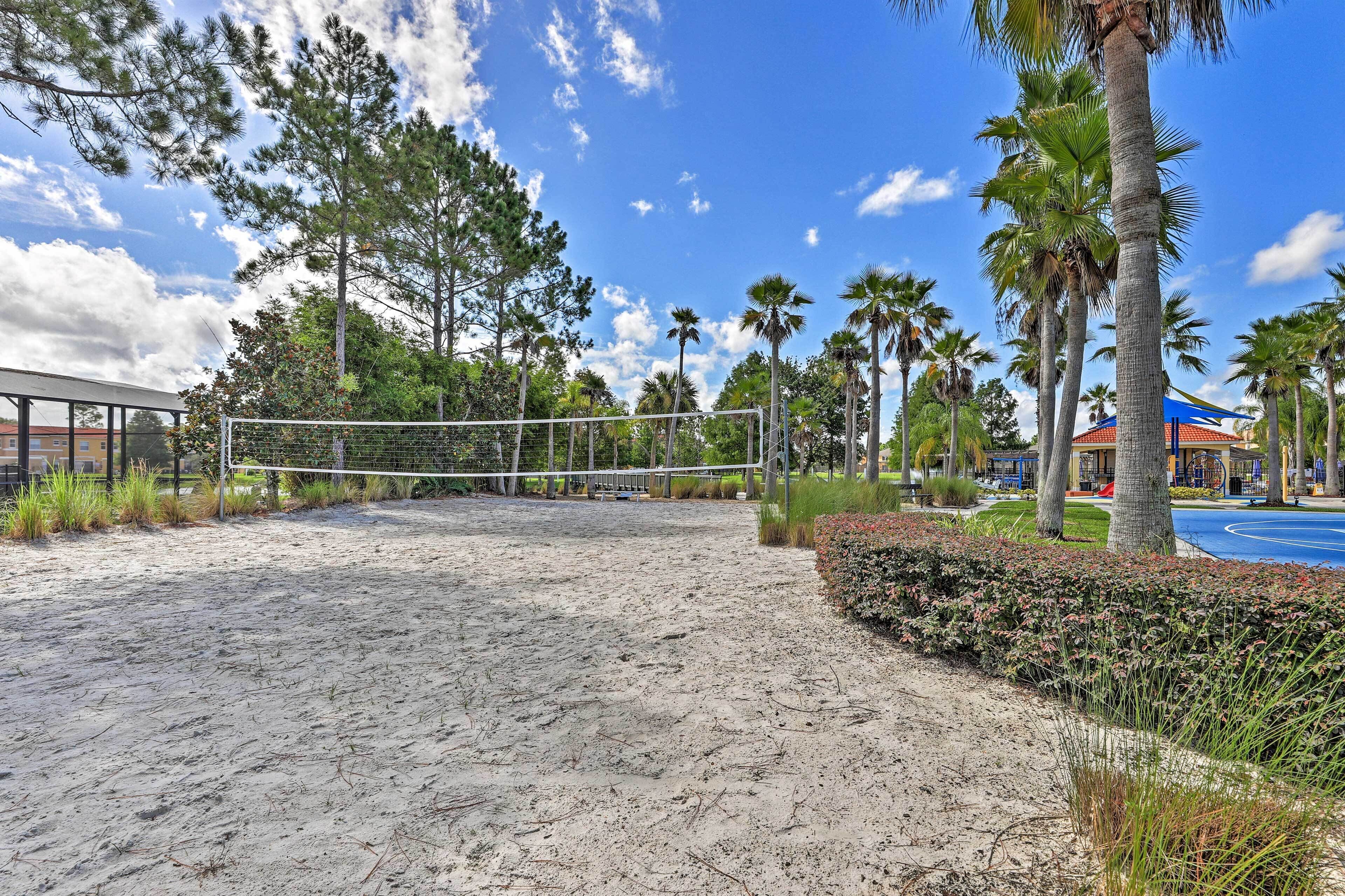 A sandy volleyball court surrounded by palm trees and a building with a blue roof.