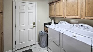 A laundry room with a white door, wooden cabinets, a washing machine, and a laundry basket. - Putting Green & Bbq: Modern Lake Havasu Oasis! (Lake Havasu City)