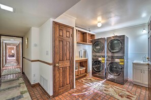 Un lavadero con dos lavadoras y secadoras de acero inoxidable, un lavabo blanco y una puerta de madera.