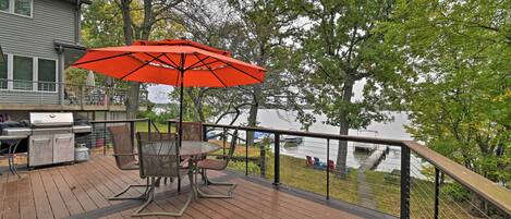 A wooden deck with outdoor furniture, a grill, and a view of a lake.