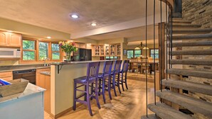 A modern kitchen with wooden cabinets, a central island with bar stools, and a stone staircase.