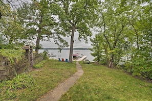 A grassy path leading to a dock with boats, surrounded by trees and a wooden fence.