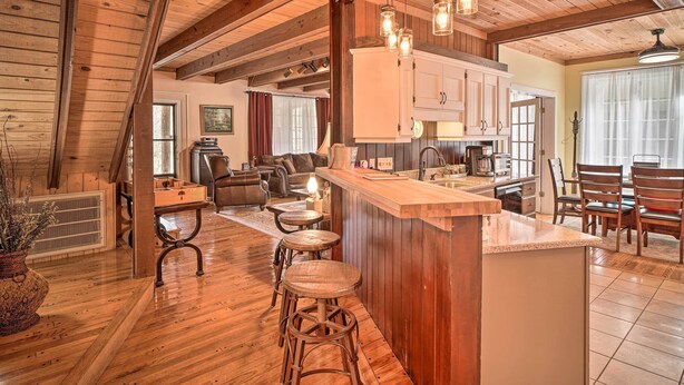 A spacious living area with a wooden ceiling, a kitchen with white cabinets, and a dining area with wooden chairs. - Tranquil Smoky Mountain Cabin w/ Porch & Fire Pit (Newport)