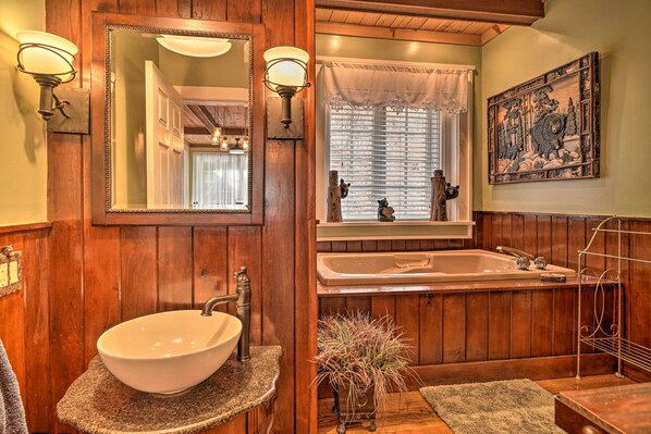 A wooden bathroom with a large sink, a bathtub, and a mirror with wall sconces.
