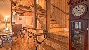 A wooden interior with a staircase, a dining area with stools, a table with a lamp, and a clock on the wall. - Tranquil Smoky Mountain Cabin w/ Porch & Fire Pit (Newport)