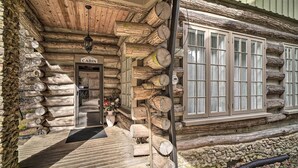 A log cabin with a 'Welcome Cabin' sign, wooden logs stacked outside, and a stone wall foundation. - Tranquil Smoky Mountain Cabin w/ Porch & Fire Pit (Newport)