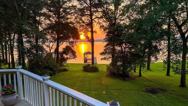 Eine Terrasse mit Blick auf einen See bei Sonnenuntergang, umgeben von Bäumen.