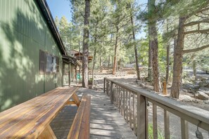 A wooden deck with benches, a metal railing, and a building with a green exterior. - Hot Tub & Patio: Pet-friendly Cabin in Munds Park! (Munds Park)