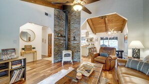 A spacious living room with a fireplace, a leather sofa, a coffee table, and a dining area visible through an open archway. - Hot Tub & Patio: Pet-friendly Cabin in Munds Park! (Munds Park)
