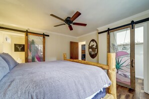A bedroom with a bed, a ceiling fan, a sliding door, and a wall with a decorative piece. - Hot Tub & Patio: Pet-friendly Cabin in Munds Park! (Munds Park)