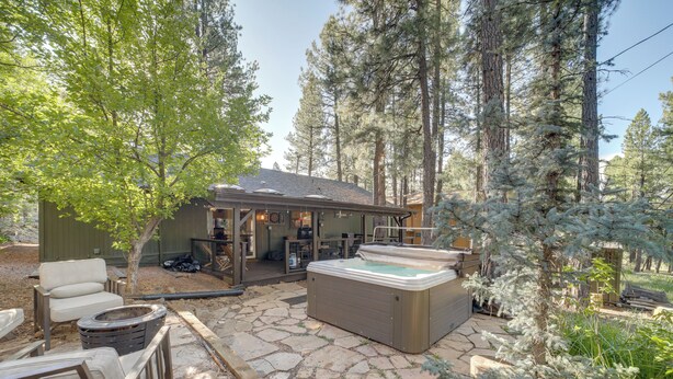 A hot tub in a forested outdoor area with stone flooring and a covered seating area. - Hot Tub & Patio: Pet-friendly Cabin in Munds Park! (Munds Park)