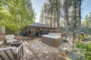 A hot tub in a forested outdoor area with stone flooring and a covered seating area. - Hot Tub & Patio: Pet-friendly Cabin in Munds Park! (Munds Park)