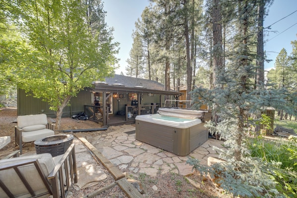 A hot tub in a forested outdoor area with stone flooring and a covered seating area.
