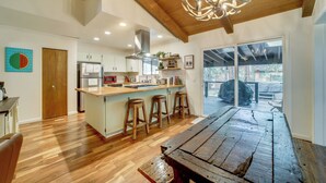A spacious kitchen with wooden flooring, a central island with stools, and a large dining table. - Hot Tub & Patio: Pet-friendly Cabin in Munds Park! (Munds Park)
