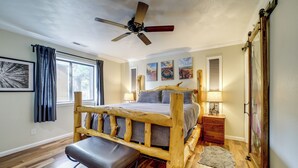 A bedroom with a wooden bed frame, a bench, a ceiling fan, and artwork on the walls. - Hot Tub & Patio: Pet-friendly Cabin in Munds Park! (Munds Park)