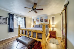 A bedroom with a wooden bed frame, a bench, a ceiling fan, and artwork on the walls.