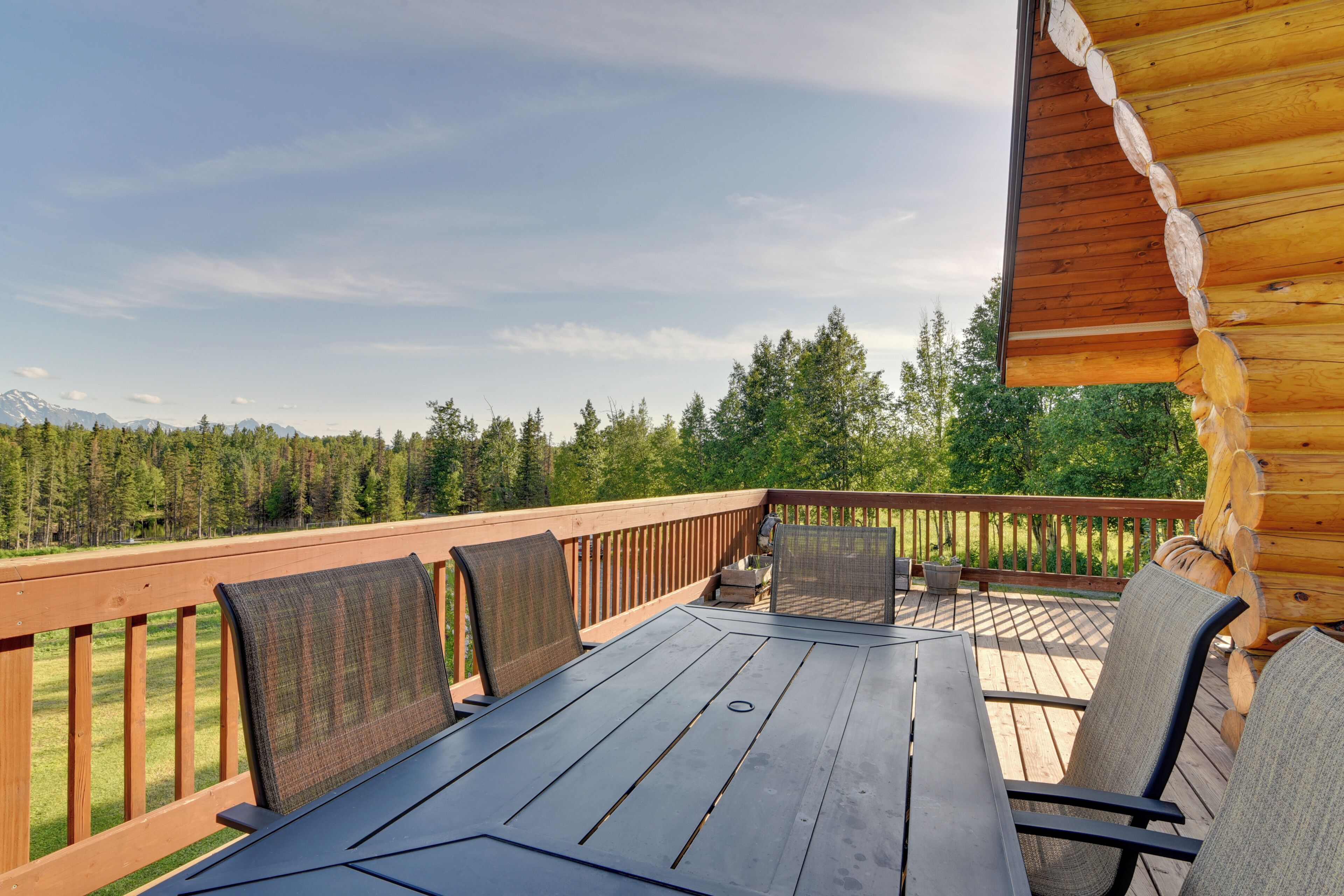 A wooden deck with a table and chairs, overlooking a forest and mountains.