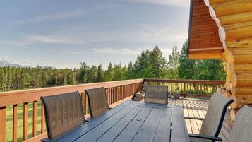 A wooden deck with a table and chairs, overlooking a forest and mountains.