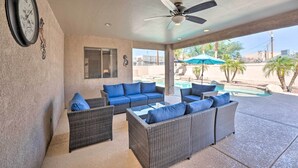 Un espacio de patio techado con mobiliario de mimbre, un ventilador de techo y vistas a una piscina.