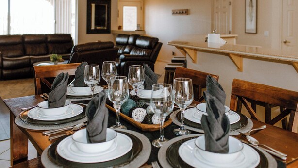 Mesa de comedor lista para seis personas, con platos, vasos y cubiertos.