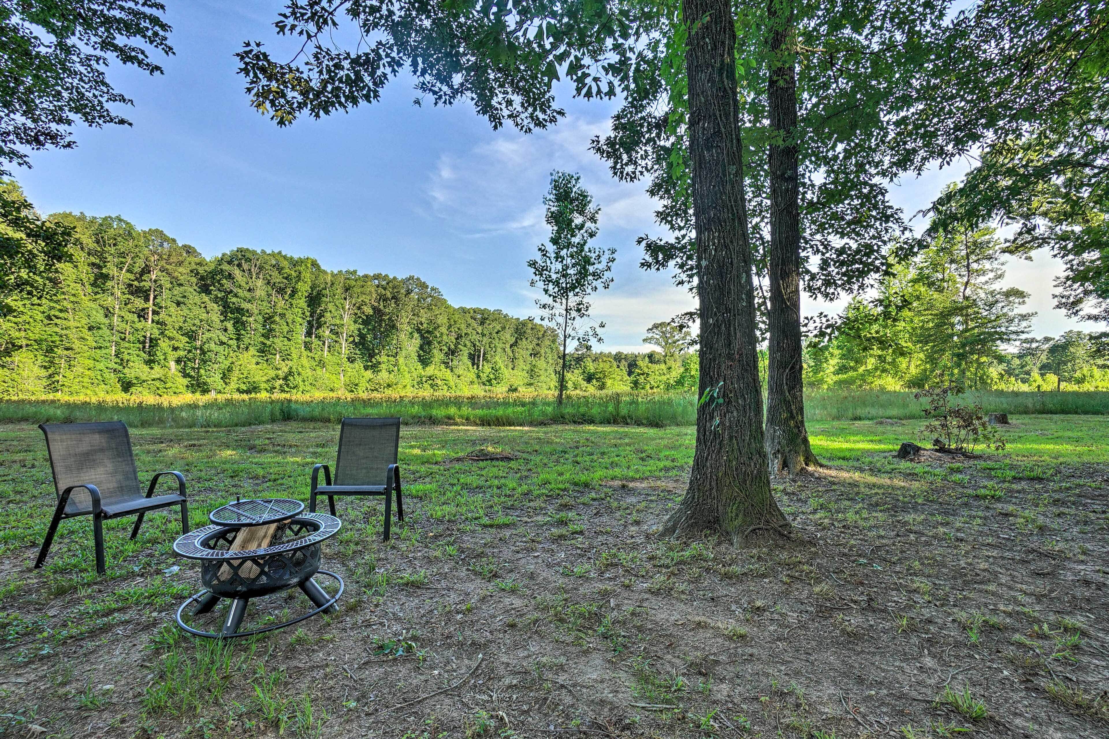 A fire pit with two chairs in a grassy outdoor area with trees in the background.
