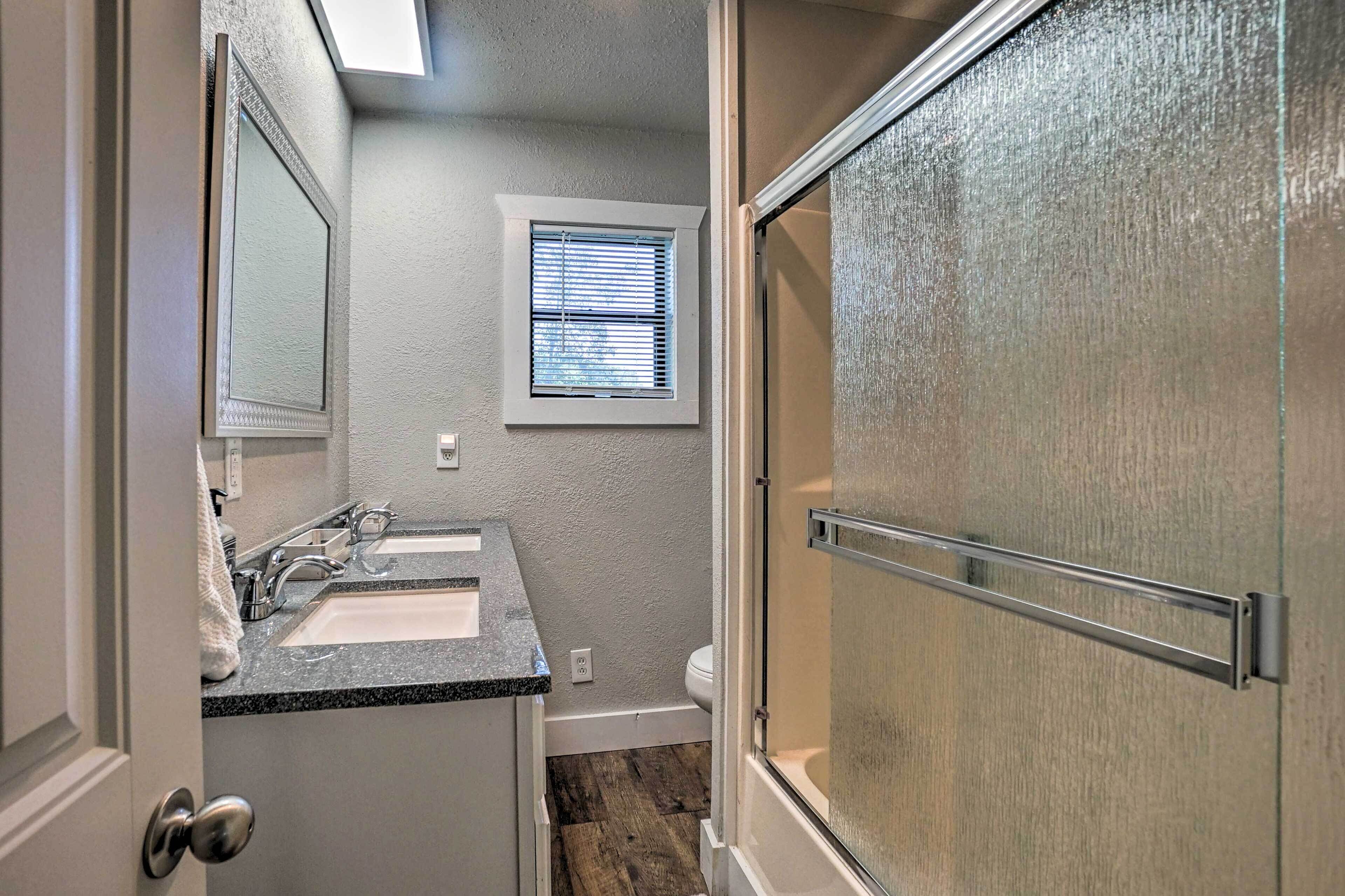 A bathroom with a double sink, a window, and a shower door.