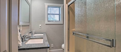 A bathroom with a double sink, a window, and a shower door.