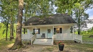 Een huis met twee verdiepingen, een veranda, een stenen fundering en een grote boom ervoor.
