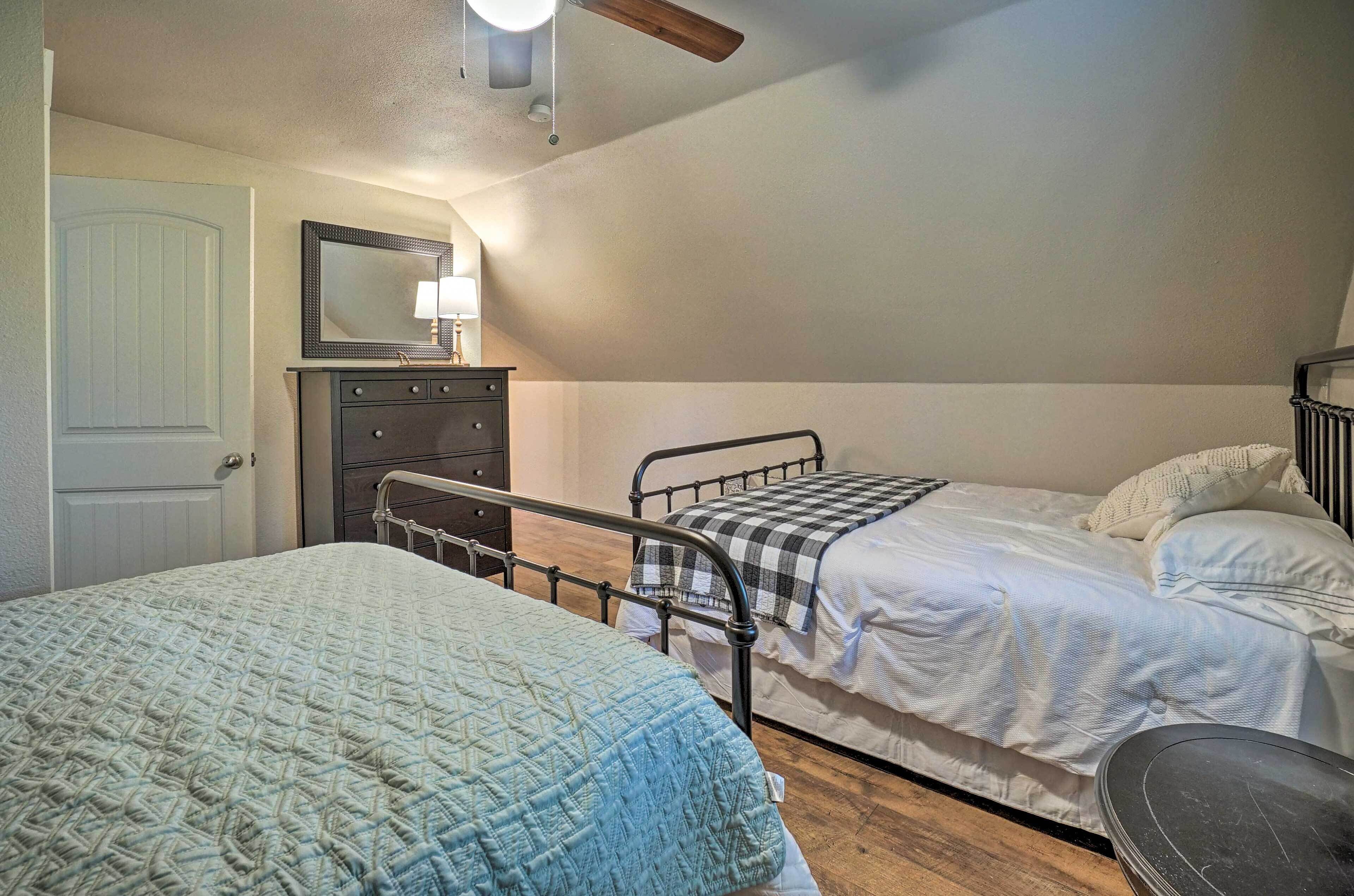 A bedroom with two beds, a dresser, a mirror, and a ceiling fan.