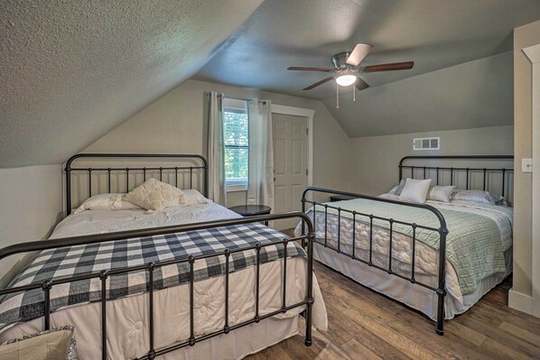 Een slaapkamer met twee bedden met metalen frame, een plafondventilator en een raam met gordijnen.