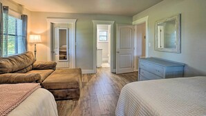 Een slaapkamer met een groot bed, een kleiner bed, een bank en een dressoir. Er is een raam met gordijnen en een lamp op een nachtkastje.