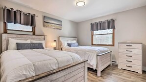 Une chambre avec deux lits, une table de chevet, une commode et un tableau au mur.