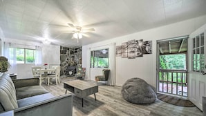 A spacious living room with a stone accent wall, a dining area, and a large window with a view of greenery. - Serene Smoky Mountain Home w/ Grill & Patio! (Topton)