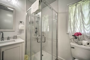 Ein modernes Badezimmer mit einer Duschkabine, einer Toilette mit Vorhang und einem Waschbecken mit Spiegel darüber.
