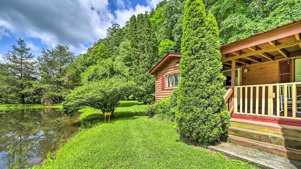 A wooden cabin with a porch, surrounded by lush greenery and a pond. - Serene Smoky Mountain Home w/ Grill & Patio! (Topton)