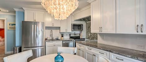 A modern kitchen with white cabinetry, stainless steel appliances, and a unique chandelier.