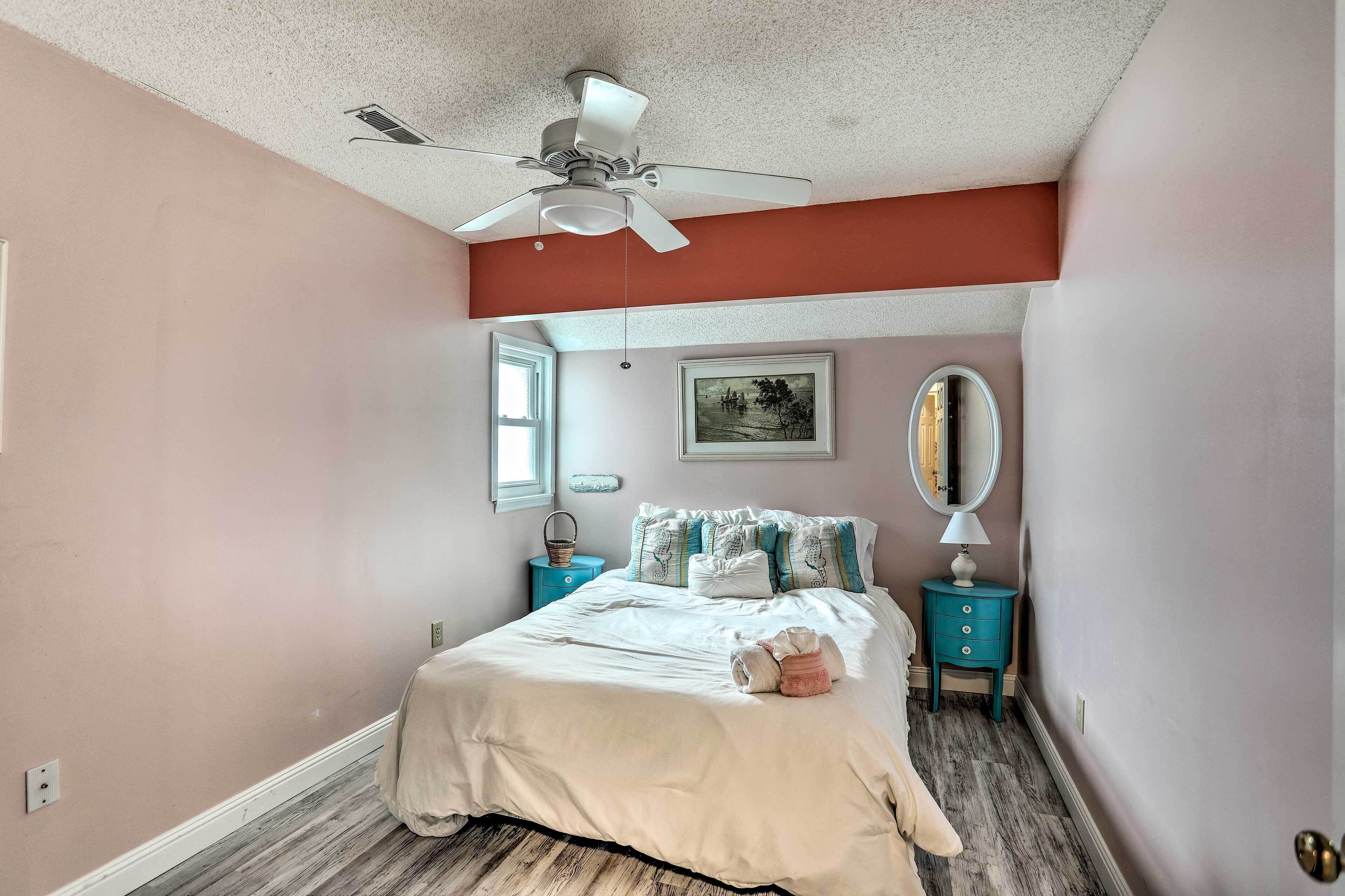 A bedroom with a bed, a ceiling fan, a nightstand, a dresser, a mirror, and a window.