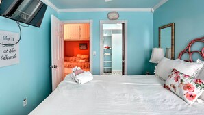 Ein Schlafzimmer mit einem Bett, einem an der Wand montierten Fernseher und einer zur Garderobe führenden Tür.